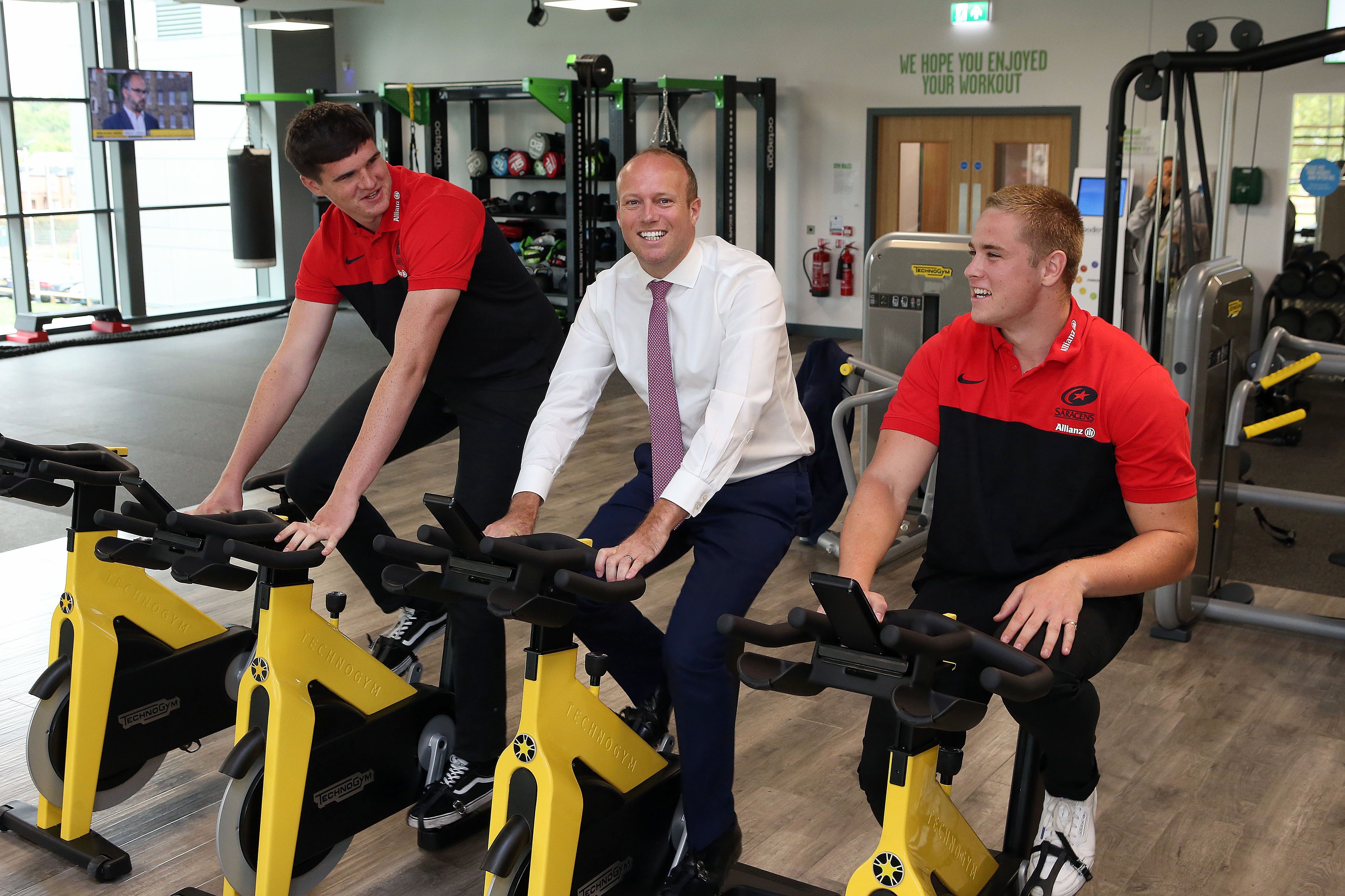 Leader of Barnet Council, Councillor Dan Thomas, with Saracens RFC players Cameron Boon (left) and Tobias Munday on the exercise bikes at New Barnet Leisure Centre.