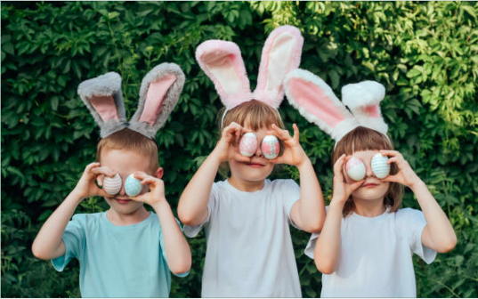 Children with bunny ears holding Easter eggs over their eyes